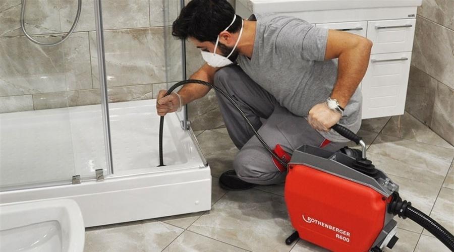 Muž čistí kanalizaci ve vaně profesionálním nářadím